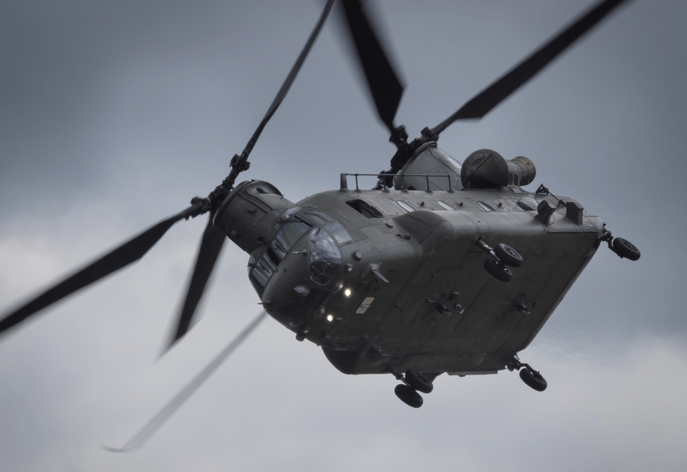A chinook helicopter in flight against a grey sky, representing the work completed by contractors in helicopter mechanic jobs overseas.
