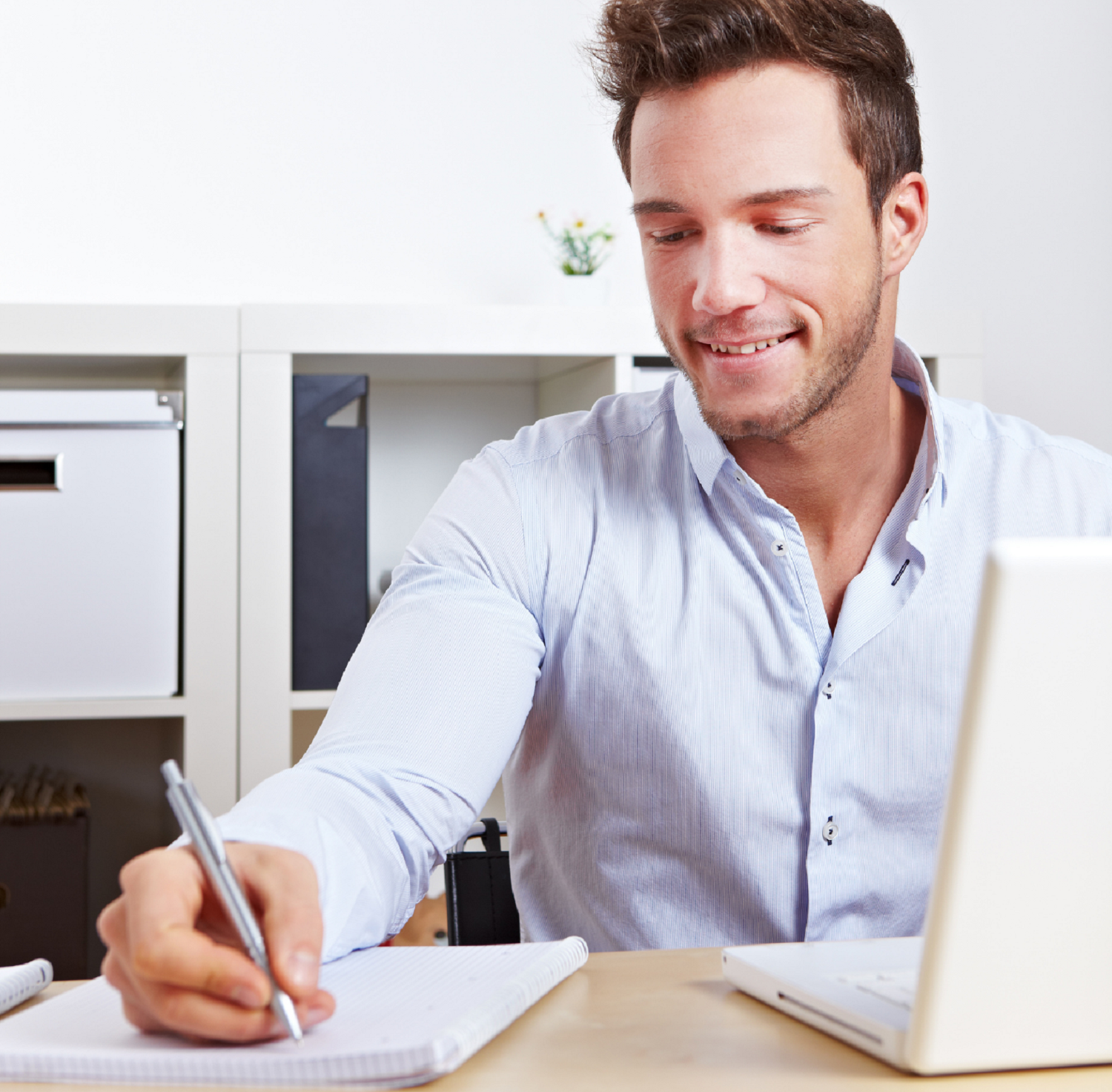 Man learning new skills, whilst writing on note pad and using a laptop